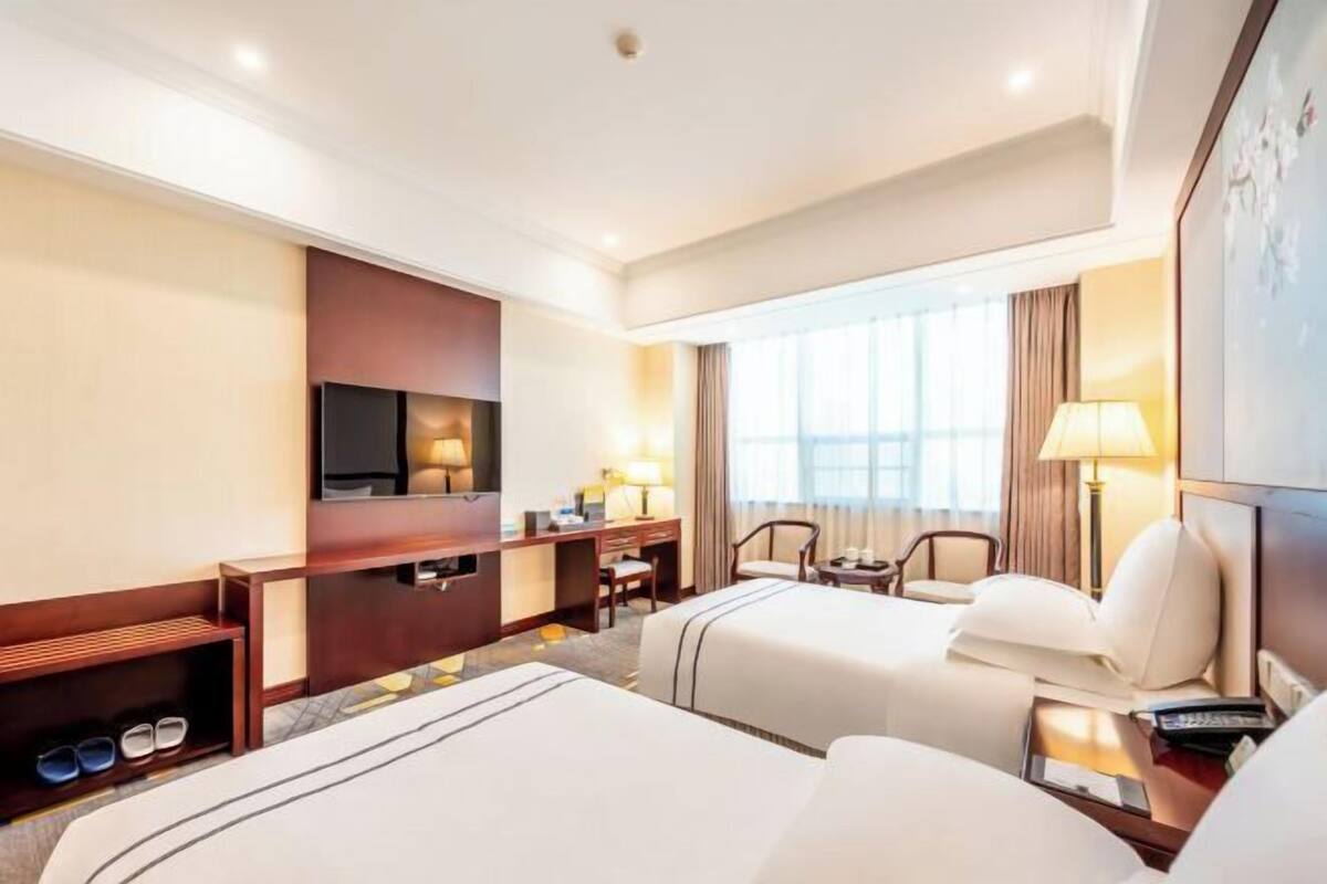A hotel room with two beds, a TV, a desk, and a chair.