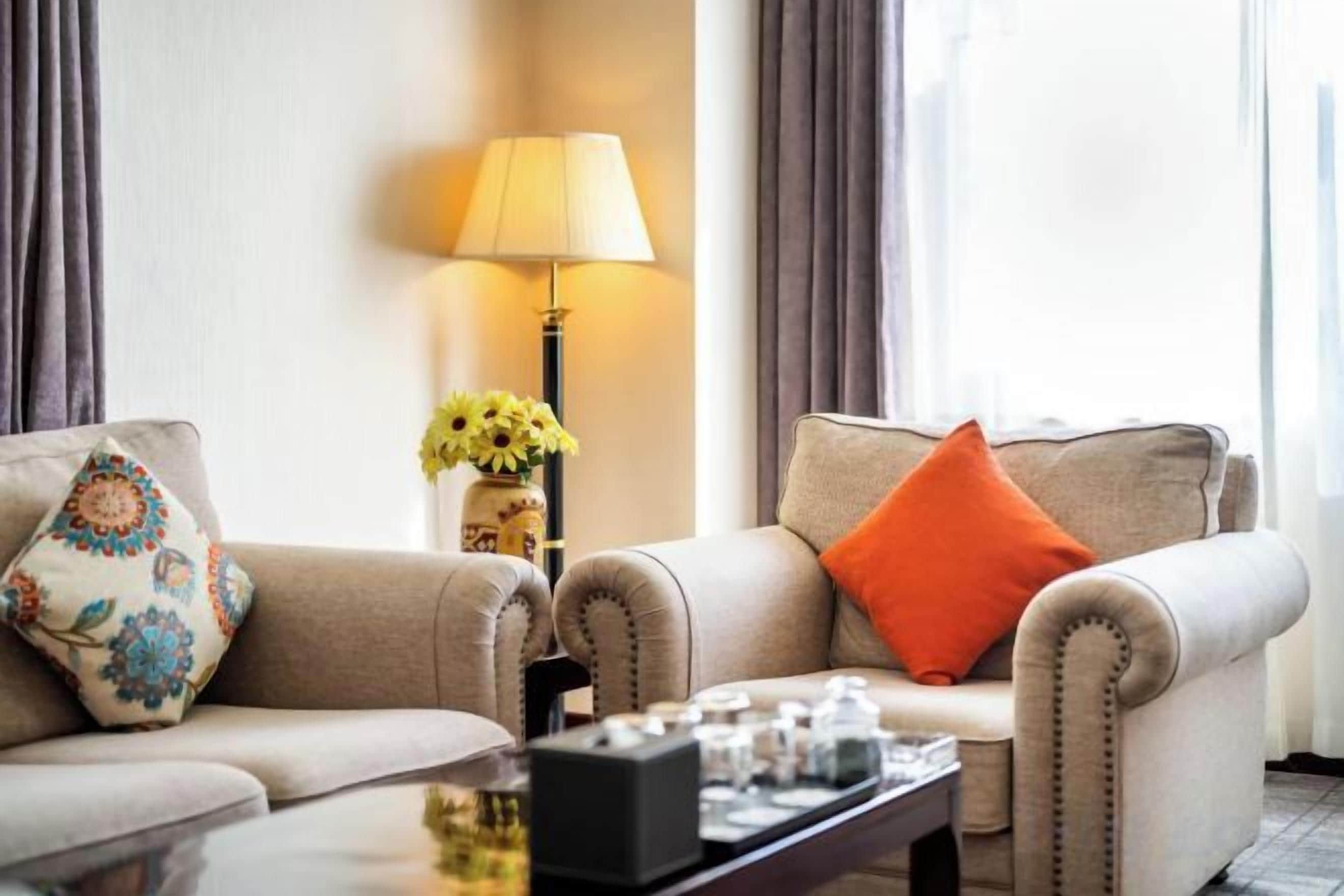 A hotel room with two sofas, a coffee table, a lamp, and a vase with flowers.