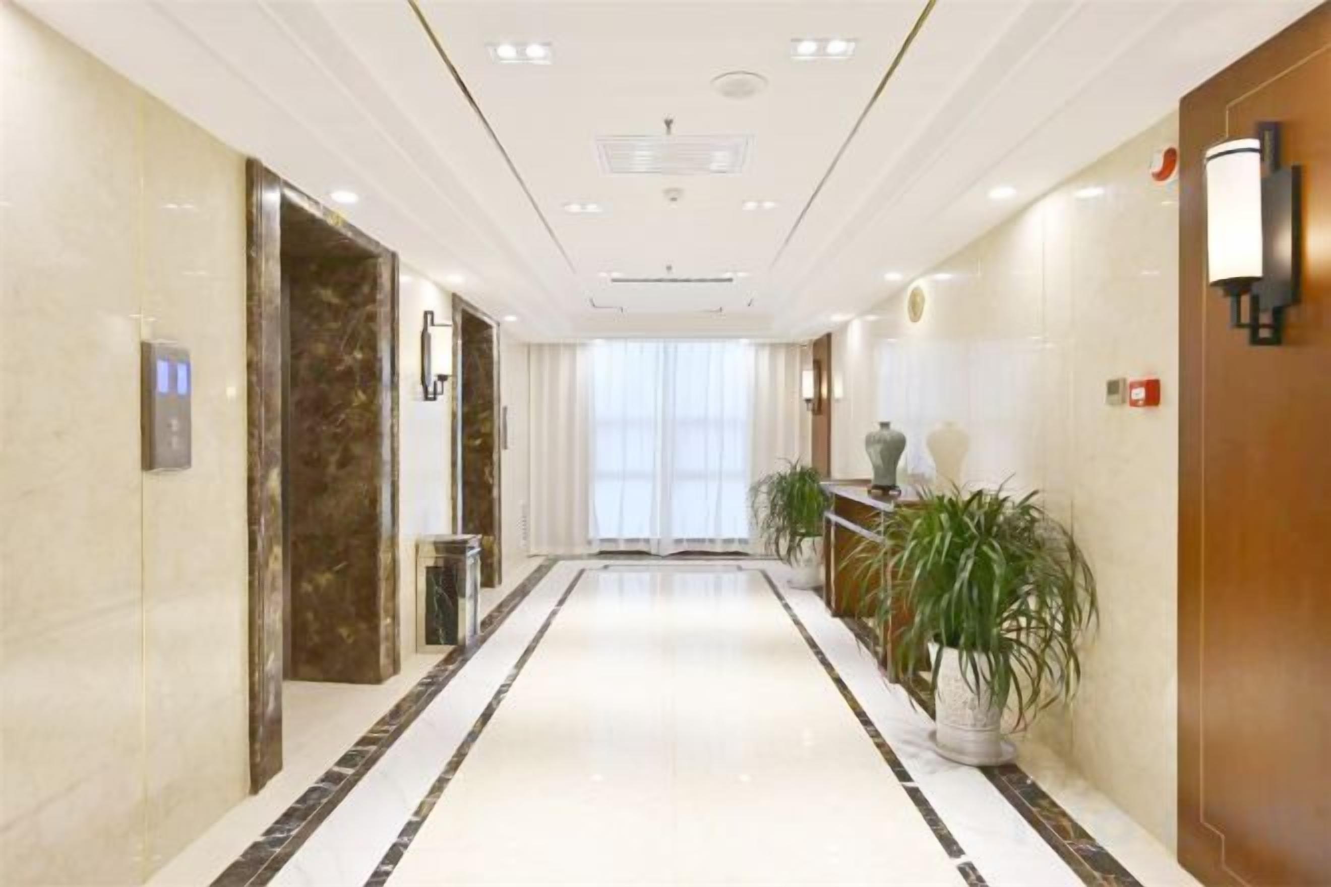 Een hotelgang met een marmeren vloer, een receptiebalie en een potplant.
