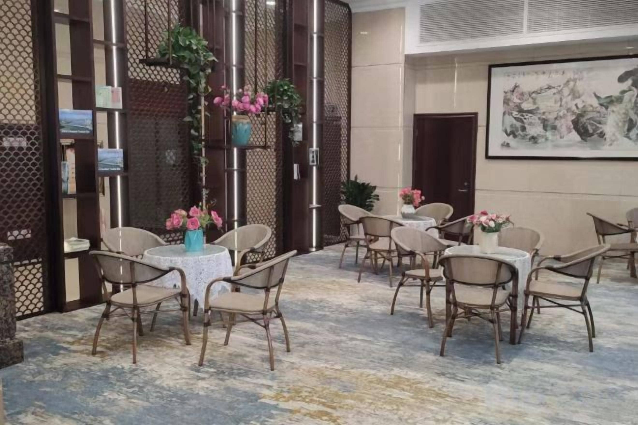Habitación de hotel con zona de estar que incluye mesas y sillas redondas, una planta decorativa y un cuadro en la pared.