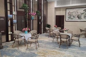 A hotel room with a seating area featuring round tables and chairs, a decorative plant, and a painting on the wall. - Post Hotel (Hanzhong)