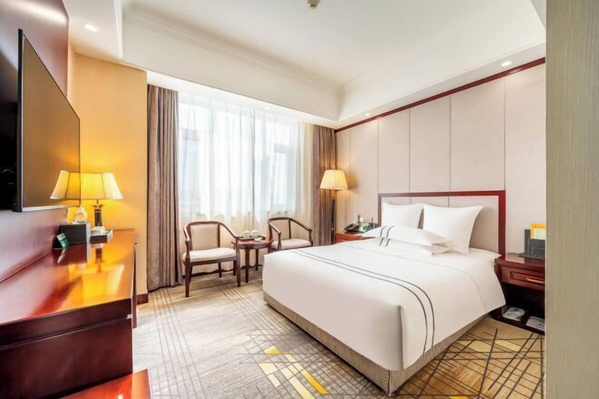 A hotel room with a large bed, a desk with a lamp, a chair, and a TV.