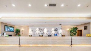 Zona de recepción moderna de un hotel, con pared de mármol, mostrador de recepción y plantas en macetas.