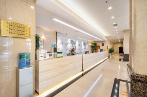 Zona de recepción de hotel con mostrador de mármol, escritorio de recepción y dispensador de agua.