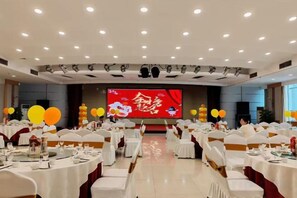 Une salle de banquet avec des tables rondes, des chaises blanches et une scène dotée d’un grand écran.