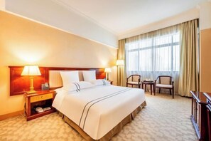 Una habitación de hotel con una cama grande, dos mesitas de noche con lámparas, un escritorio pequeño y una silla.