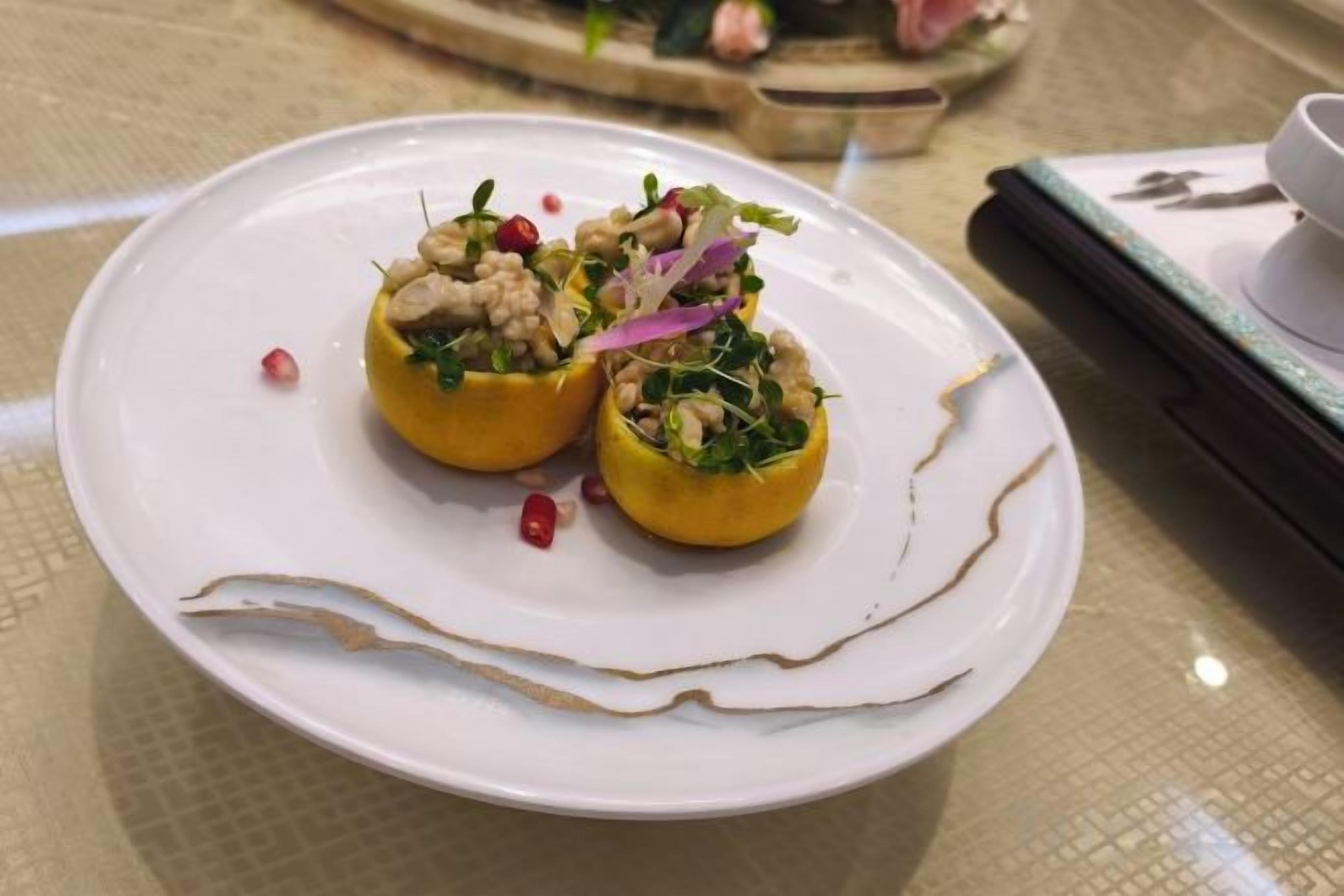 A white plate with two stuffed yellow peppers garnished with nuts and vegetables, placed on a table with a patterned tablecloth.