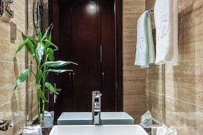 Un baño con un espejo grande, un lavabo, una planta y un perchero para toallas.