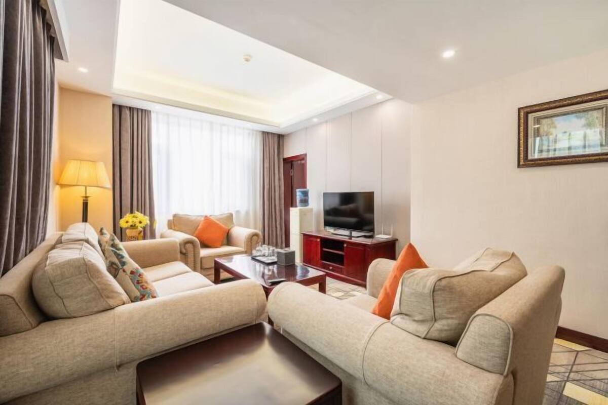 A hotel room with a sofa set, a TV, a lamp, and a painting on the wall.