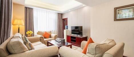 A hotel room with a sofa set, a TV, a lamp, and a painting on the wall.