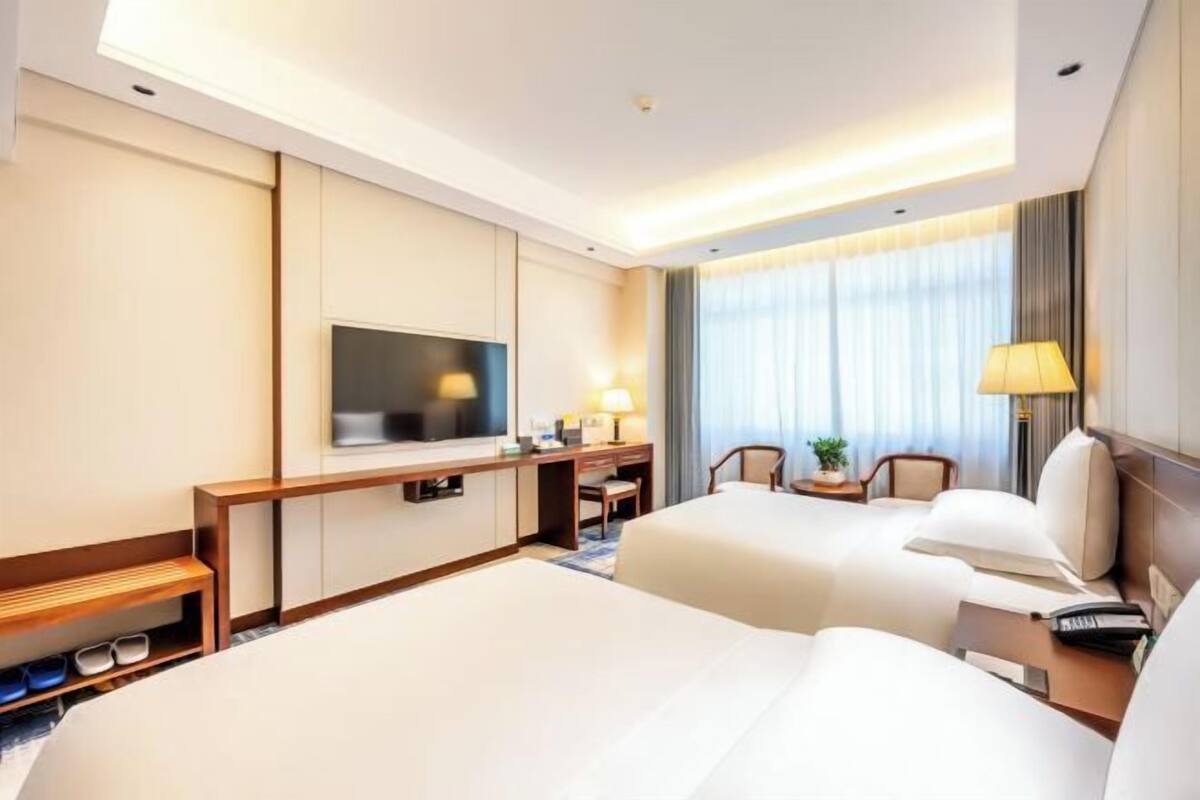 A hotel room with two beds, a TV, a desk, and a chair.