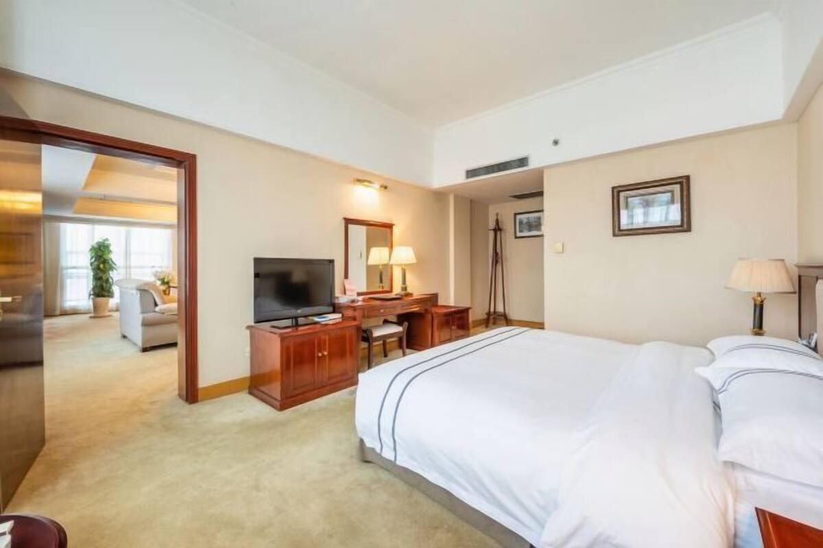 A hotel room with a large bed, a desk with a computer, a television, and a lamp.