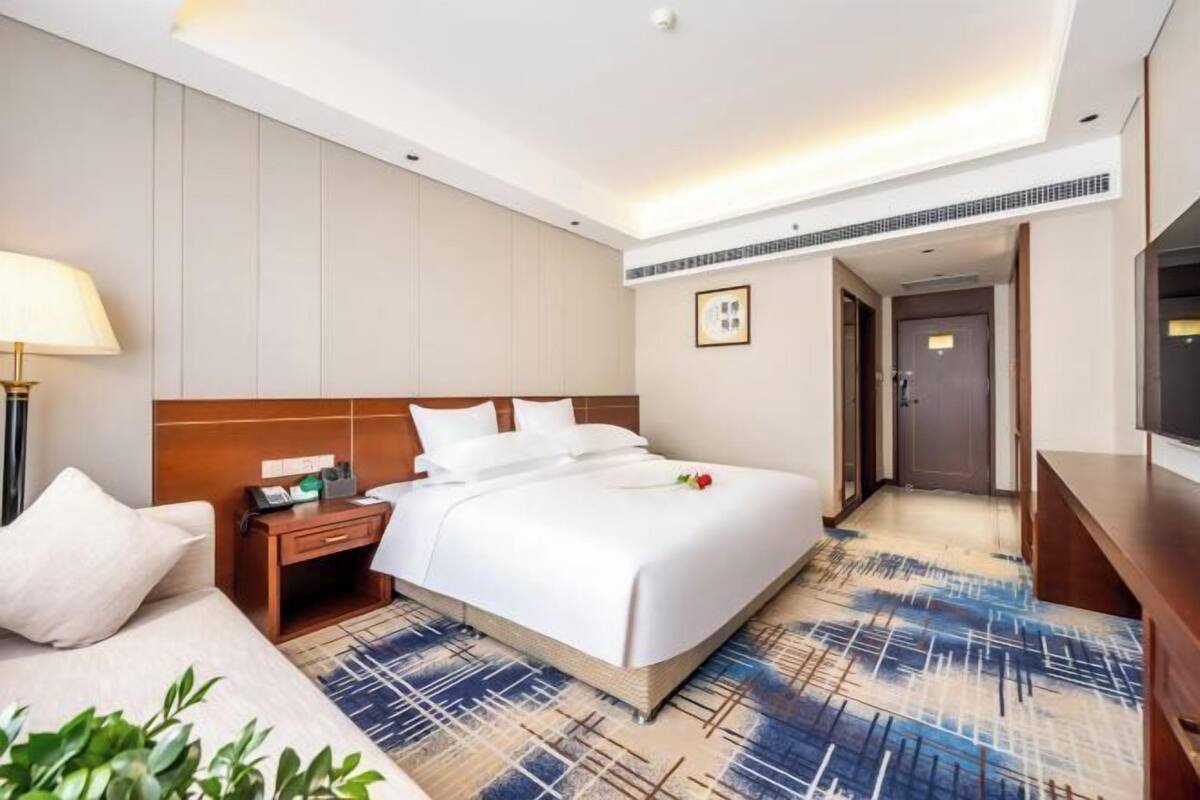 A hotel room with a bed, bedside table, lamp, and a TV.