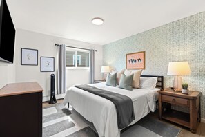 Quarto moderno com cama, mesas de cabeceira, escrivaninha e uma janela grande.