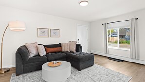 A modern living room with a sectional sofa, a round coffee table, and a floor lamp. - Contemporary 1BR, Fast WiFi, Pet-Friendly (Mount Clemens)