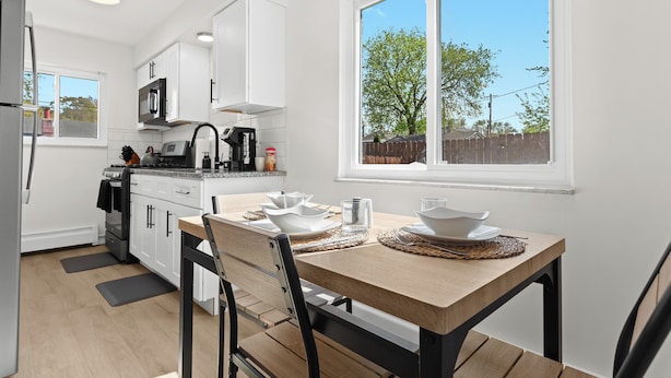 A modern kitchen with white cabinets, a wooden dining table, and a large window. - Contemporary 1BR, Fast WiFi, Pet-Friendly (Mount Clemens)