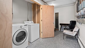 A laundry room with a washing machine, a dryer, a wooden door, a chair, and a wall-mounted water heater. - Contemporary 1BR, Fast WiFi, Pet-Friendly (Mount Clemens)