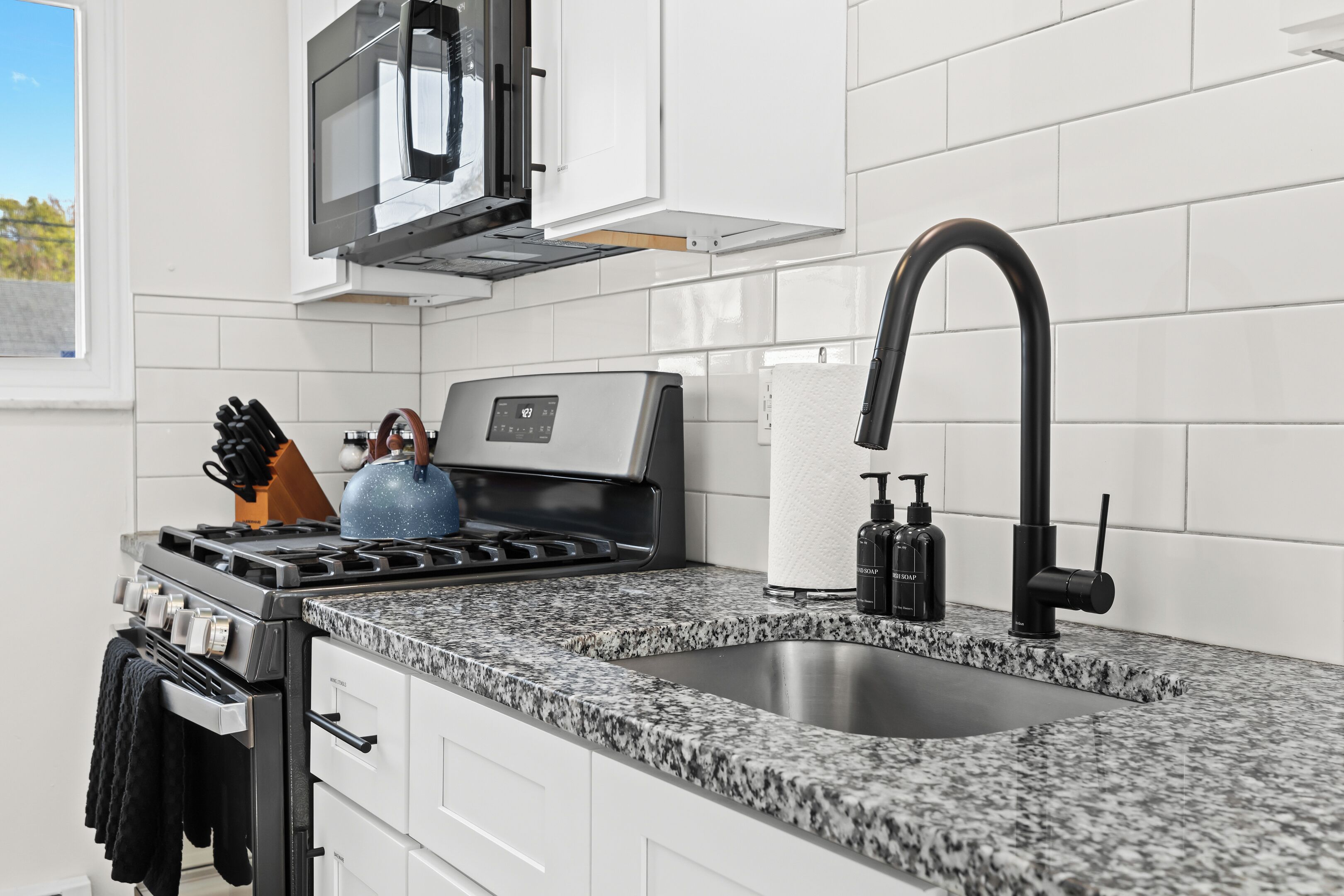 A modern kitchen with white cabinets, a granite countertop, a stainless steel stove, a black faucet, and a microwave above the stove.