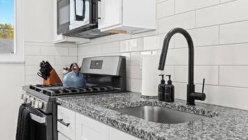 A modern kitchen with white cabinets, a granite countertop, a stainless steel stove, a black faucet, and a microwave above the stove.