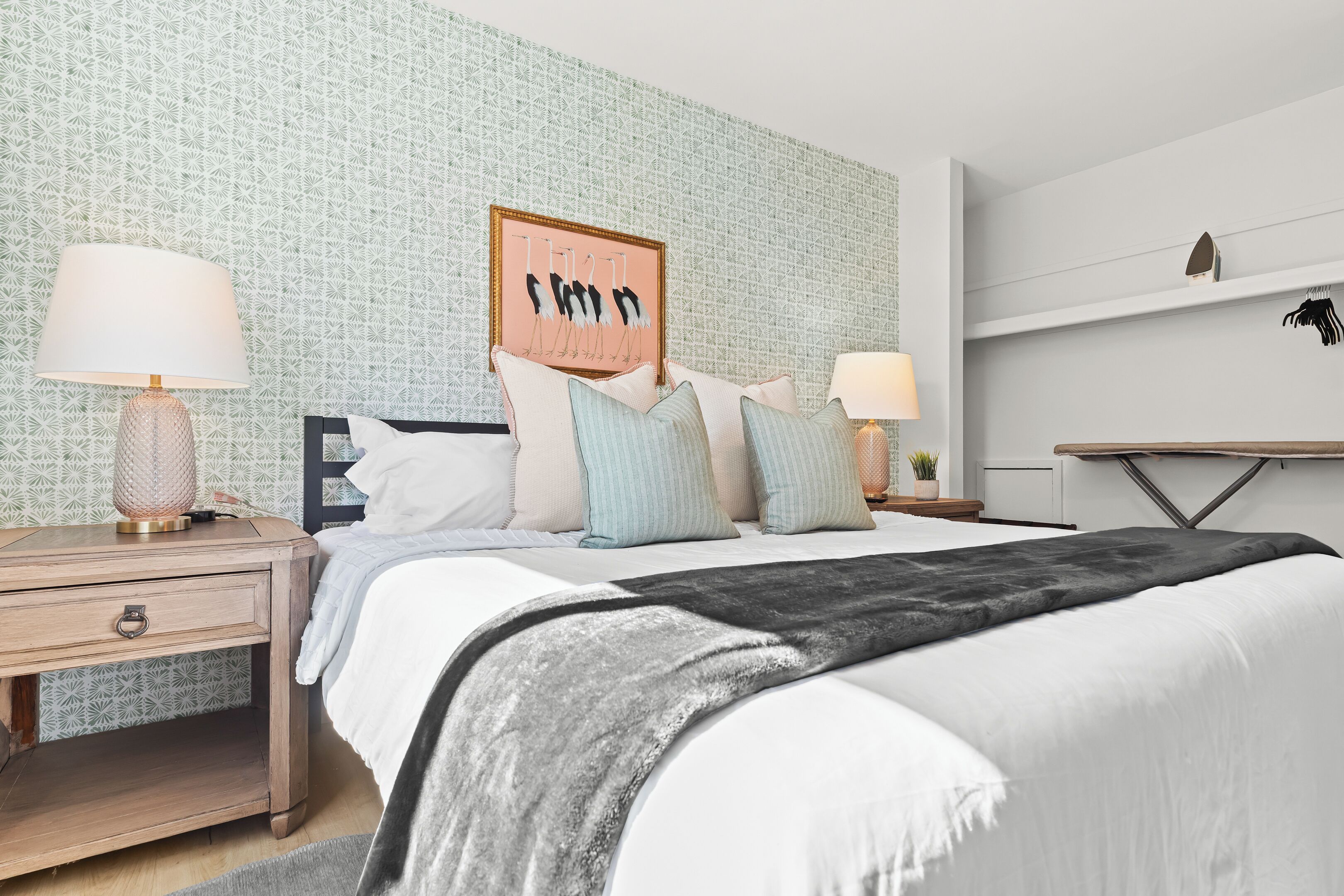 A neatly arranged bedroom with a bed, bedside tables, and a wall-mounted shelf.