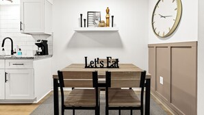 A modern kitchen with white cabinetry, a wooden dining table, and a clock on the wall. - Cozy Modern 1BR Close to Downtown (Mount Clemens)