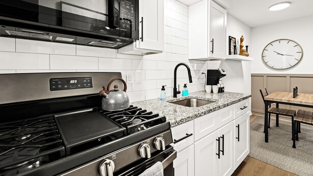 A modern kitchen with white cabinets, a stainless steel stove, a microwave, and a sink. - Cozy Modern 1BR Close to Downtown (Mount Clemens)