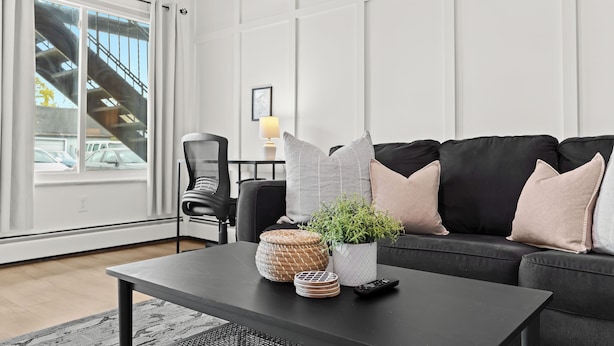 Una sala de estar moderna con un sofá negro, una mesa de centro, una silla y un ventanal con vistas a una escalera.