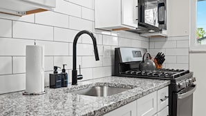 Una cocina moderna con armarios blancos, encimera de granito, pileta de acero inoxidable, grifo negro, estufa a gas y microondas.