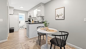 A modern kitchen with white cabinets, a central island, and a dining area with a round table and chairs. - Quiet Cozy End Unit Near Mt. Clemens Downtown (Mount Clemens)