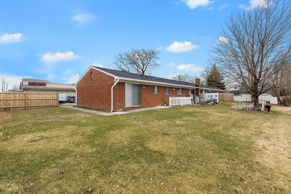 A single-story brick building with a gabled roof, a front porch, and a fenced backyard.