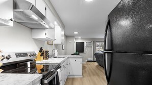A modern kitchen with white cabinetry, a black refrigerator, and a stainless steel range hood.