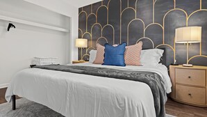 Een moderne slaapkamer met een groot bed, twee nachtkastjes met lampen, een muur met een geometrisch patroon en een radiator.