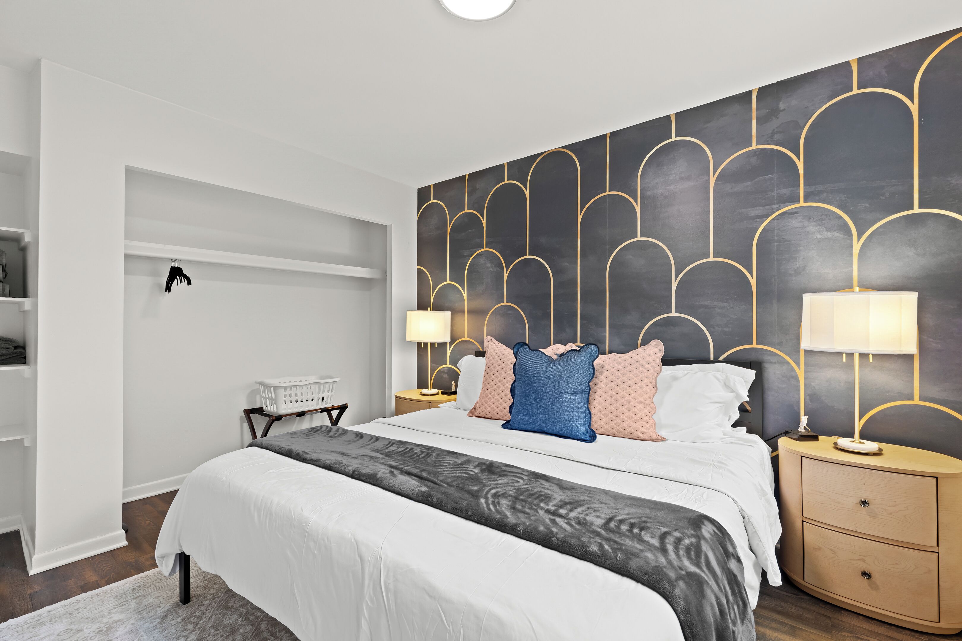 A modern bedroom with a large bed, two bedside tables with lamps, a wardrobe, and a unique wall design.