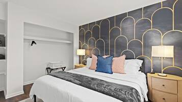 A modern bedroom with a large bed, two bedside tables with lamps, a wardrobe, and a unique wall design.