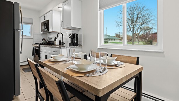 Een moderne keuken met witte kasten, een eettafel gedekt voor vier personen, en een groot raam met uitzicht op de omgeving.