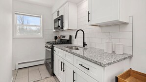 Una cocina moderna con armarios blancos, encimera de granito, pileta de acero inoxidable y microondas.