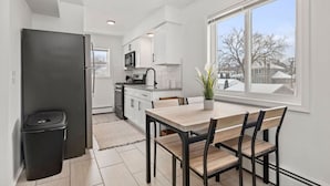 Una cocina moderna con armarios blancos, un refrigerador negro y una zona de comedor con una mesa y sillas de madera.