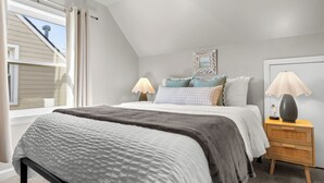 Een slaapkamer met een bed, twee nachtkastjes, een raam met gordijnen en een schilderij aan de muur.