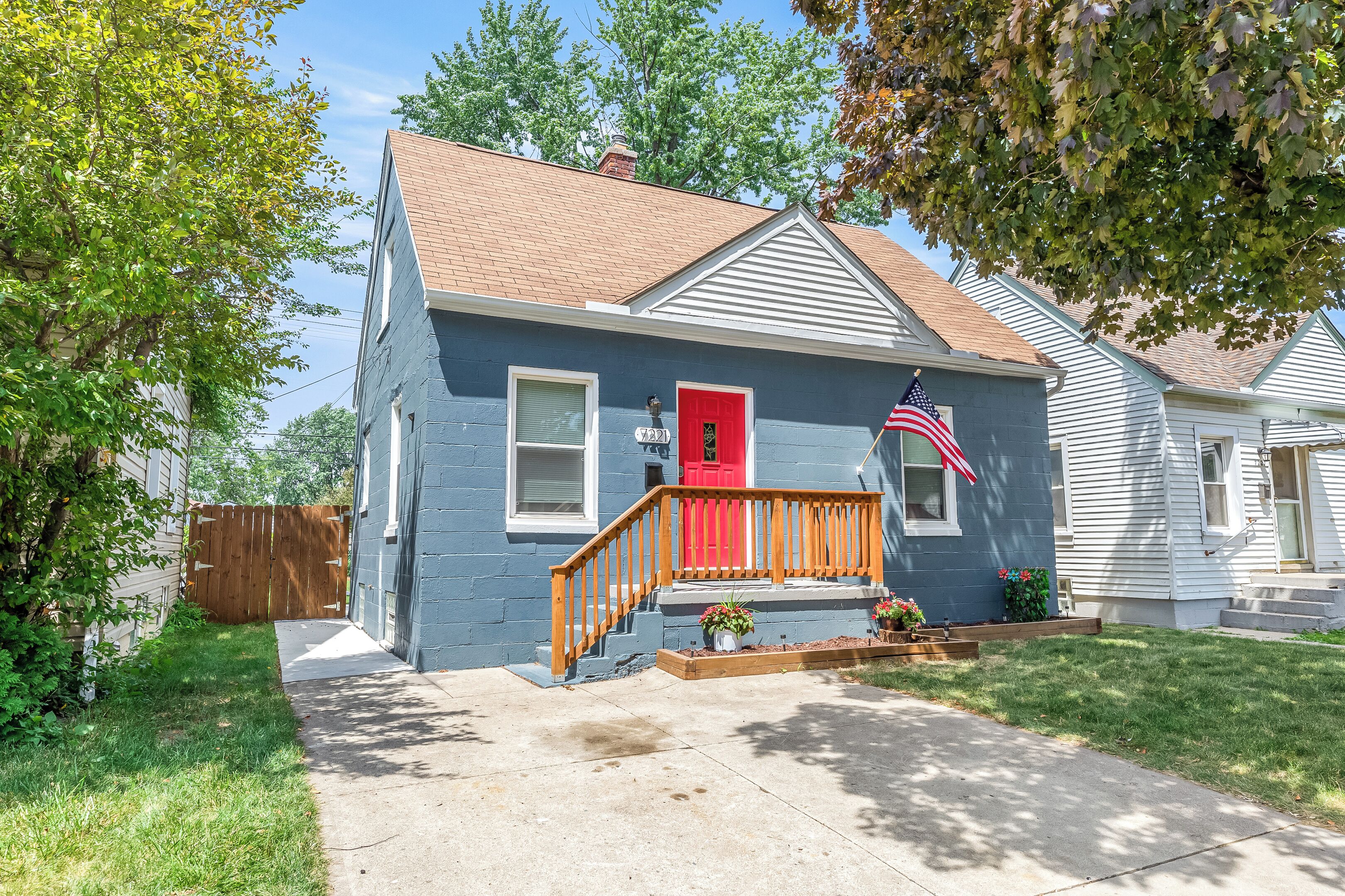 A two-story house with a red front door, a wooden front porch, and a small front yard with a flag.