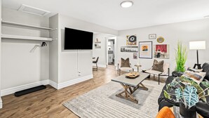 Una sala de estar moderna con una televisión de pantalla plana, una mesa de comedor y un sofá. Hay cuadros en la pared y una planta en la esquina.