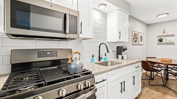 Una cocina moderna con electrodomésticos de acero inoxidable, armarios blancos y encimera de granito.