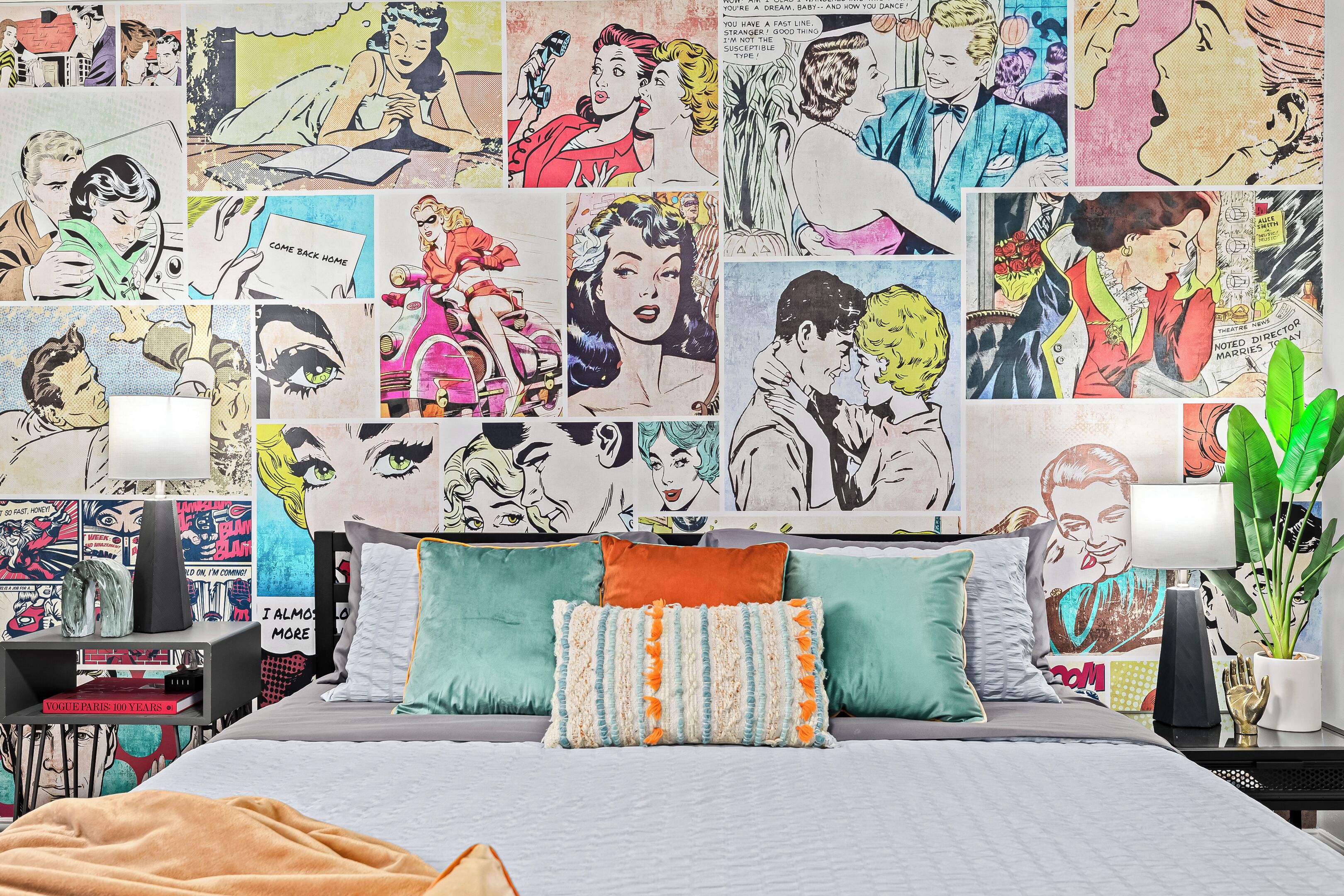 Ein Schlafzimmer mit einem Bett, Kissen, einem Nachttisch, einer Lampe und einer Wand mit Comic-Kunstwerken.