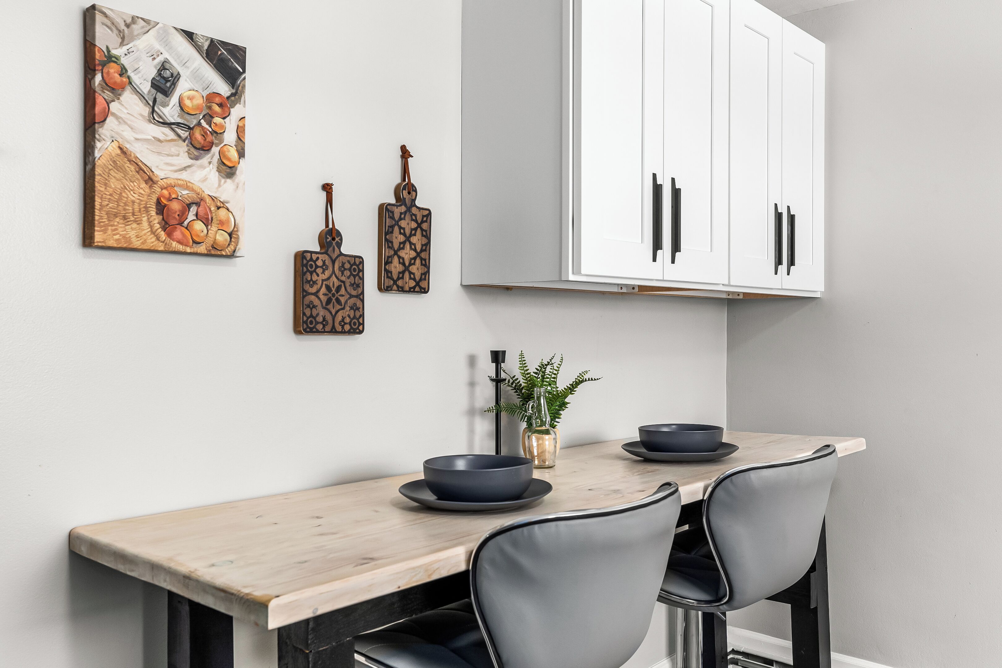 Un'area pranzo con tavolo in legno, due sedie, un vaso con una pianta e un quadro appeso al muro.