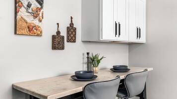 Un'area pranzo con tavolo in legno, due sedie, un vaso con una pianta e un quadro appeso al muro.