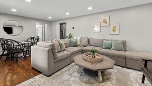 Una sala de estar moderna con un sofá modular, una mesa de comedor con sillas, una mesa de centro y un espejo grande en la pared.