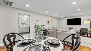 Un comedor moderno con una mesa redonda para cuatro personas, un sofá y un televisor montado en la pared.