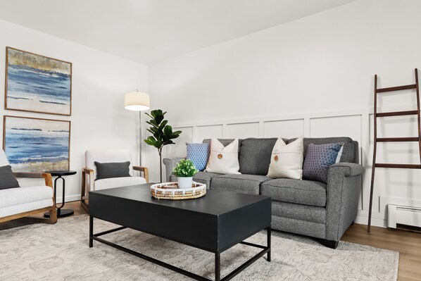 Una sala de estar moderna con un sofá gris, una mesa de centro negra y un sillón blanco.
