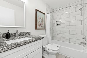 Un baño moderno con encimera de granito, inodoro blanco y ducha a ras de suelo con puerta de cristal.
