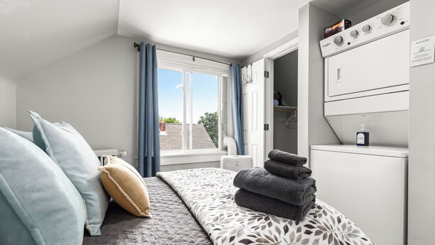 Un dormitorio con cama, almohadas, una ventana con cortinas, una lavadora y un letrero de lavandería.