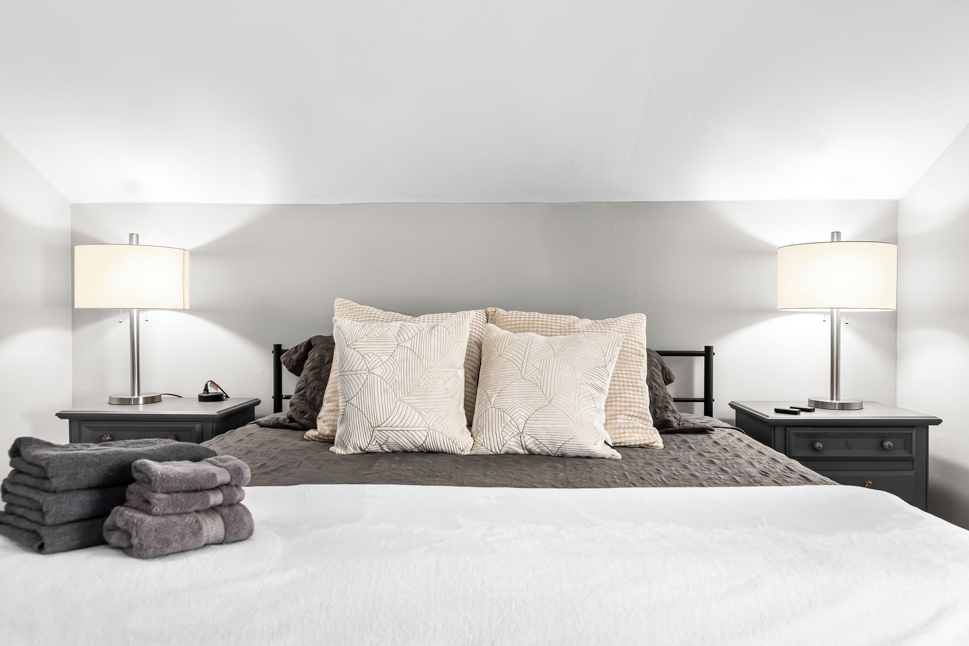 Un lit bien fait, recouvert d’une couette blanche, avec deux lampes de chevet et une pile de serviettes pliées.